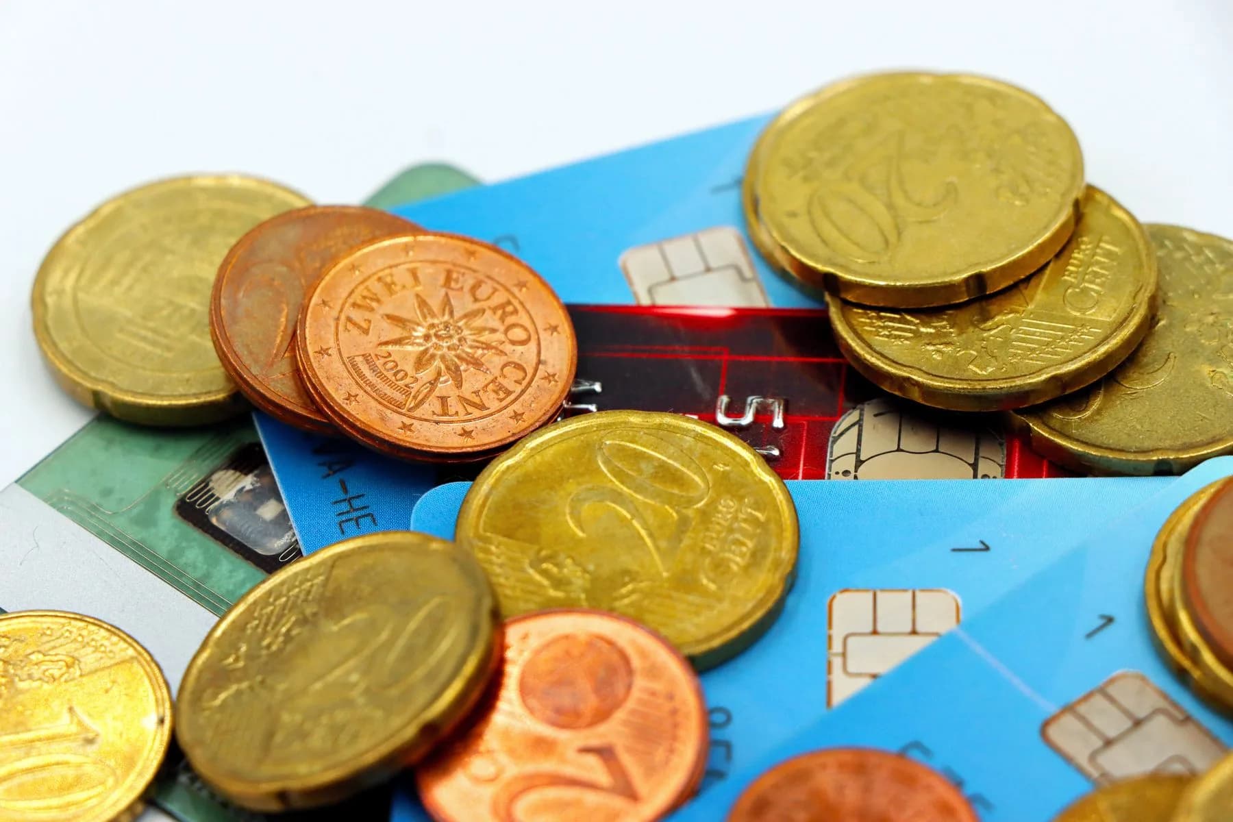 Euromuenzen liegen auf mehreren Bankkarten mit Chip vor weissem Hintergrund
