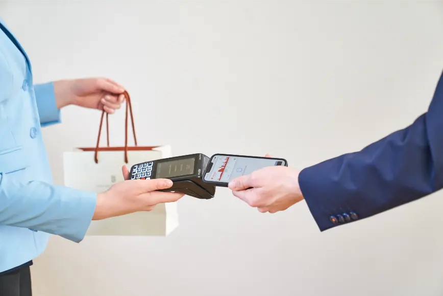 Verkäuferin hält einem Kunden das Kartenterminal hin, der mit dem Smartphone bezahlt.