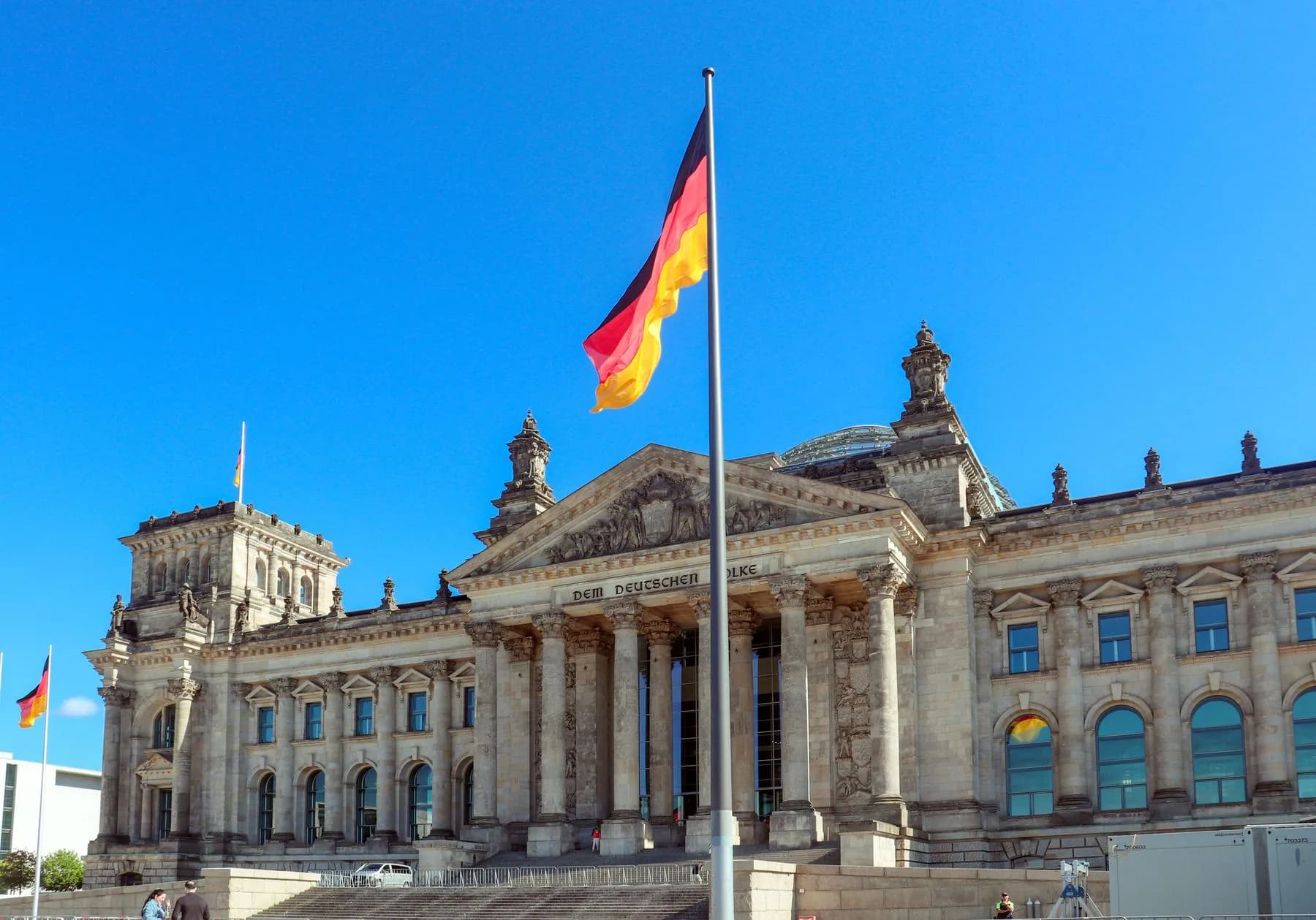 Reichstagsgebaeude in Berlin mit wehender Deutschlandflagge vor blauem Himmel