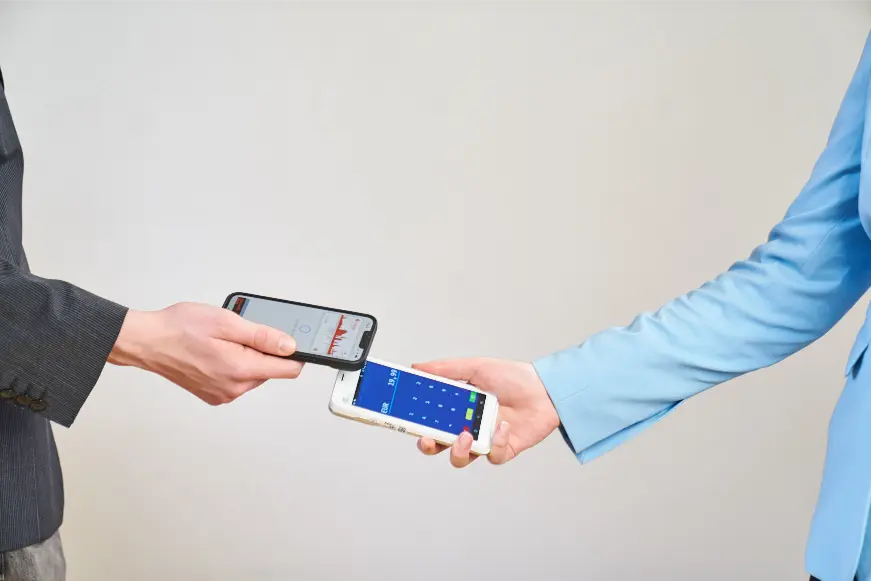 Ein Smartphone dient als Kartenterminal und zeigt den Betrag, ein zweites Handy bezahlt kontaktlos.