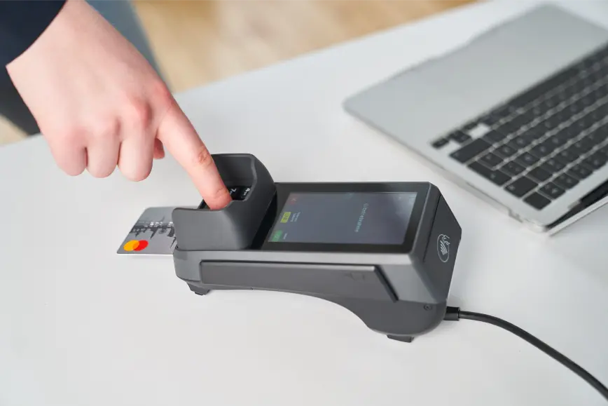 Hand bedient ein stationäres Kartenterminal am Schreibtisch, eine Mastercard steckt im Chipleser